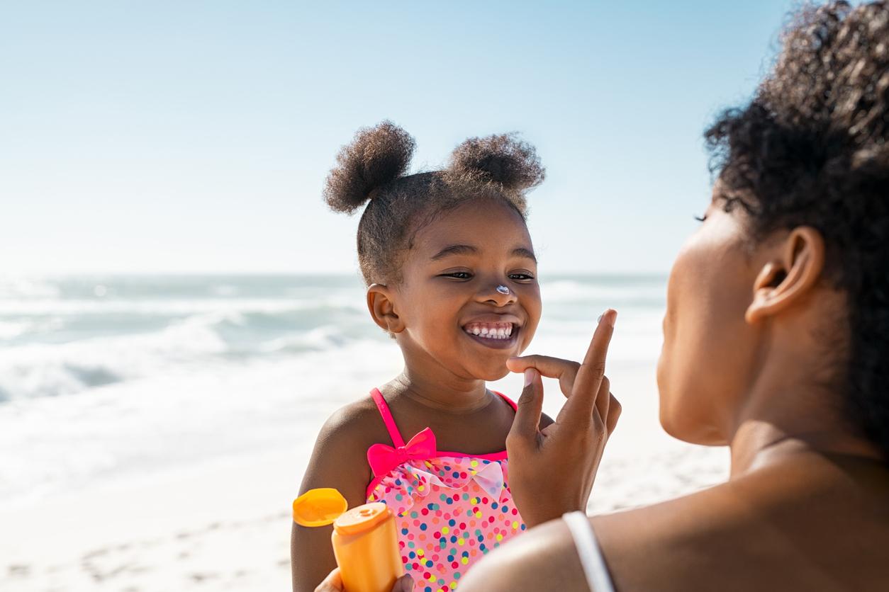 Pretty black mom applies sunscreen to adorable little black girl while at the beach